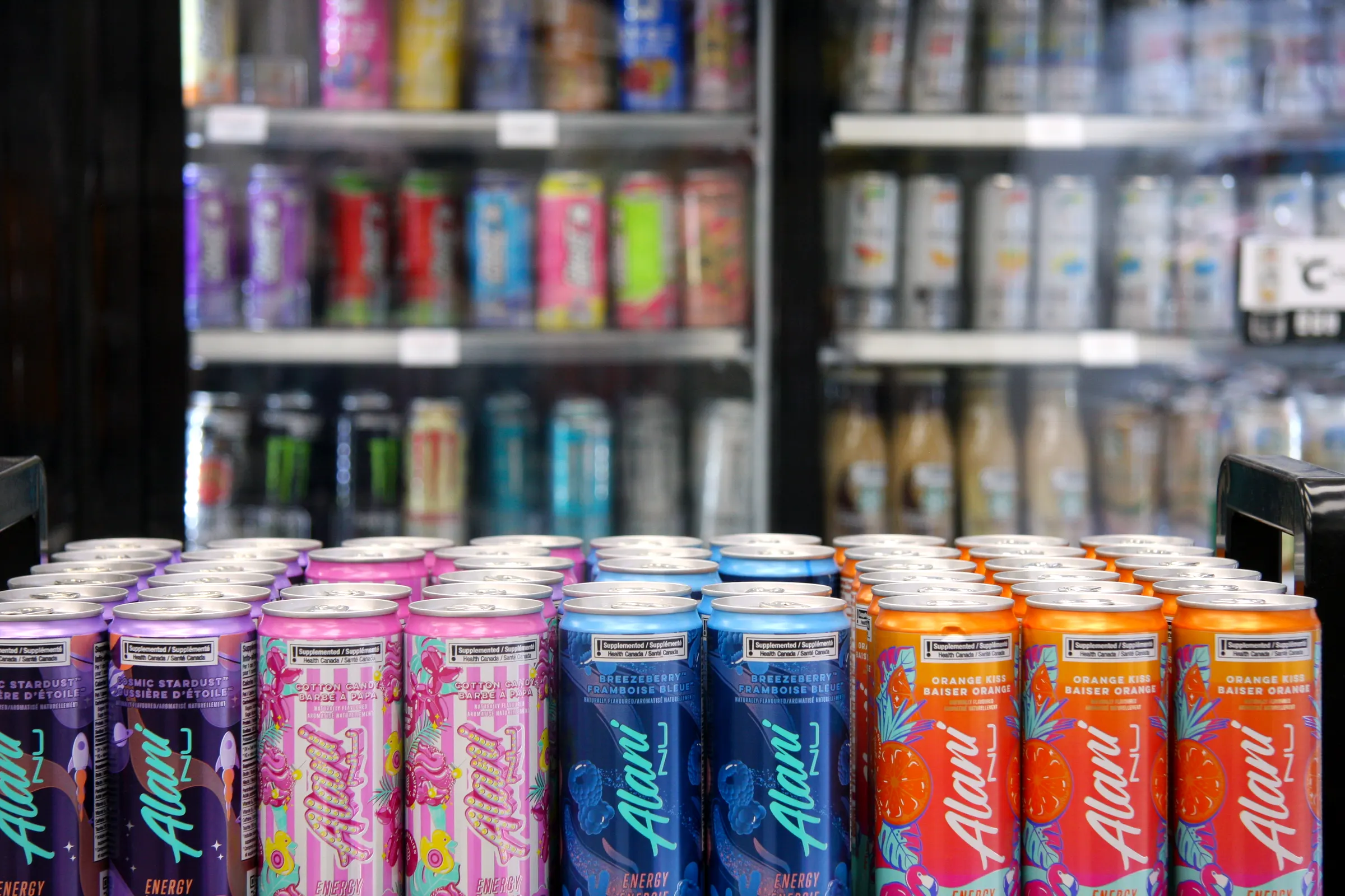 The energy cans from a low angle, the lit cooler shelves rising behind the display.