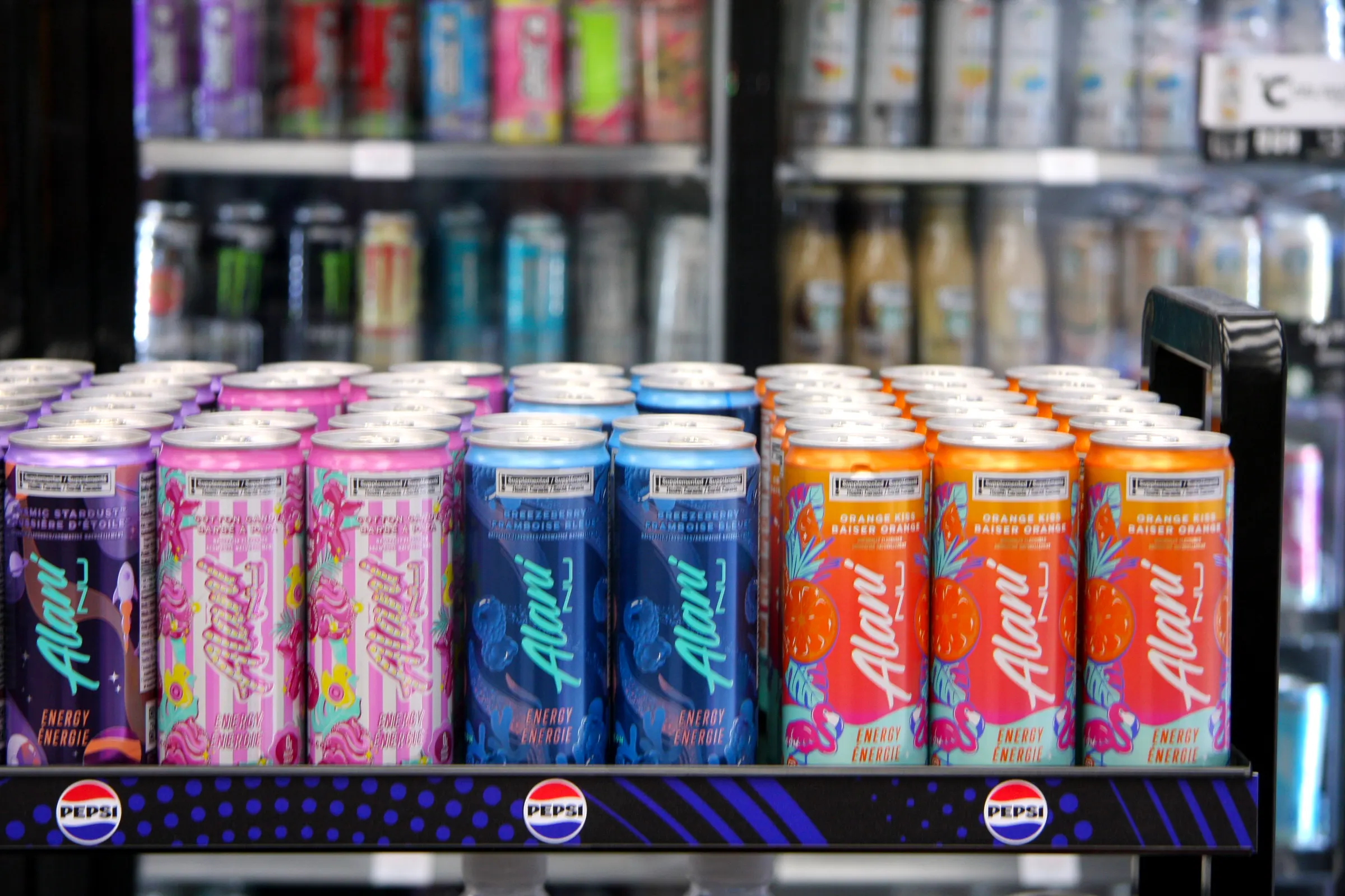 Rows of energy cans across the branded floor display, colours running pink through blue to orange.
